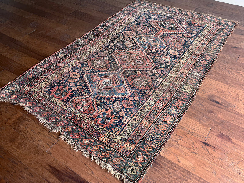 an antique shiraz qashqai rug with a dark blue field and brick red medallions