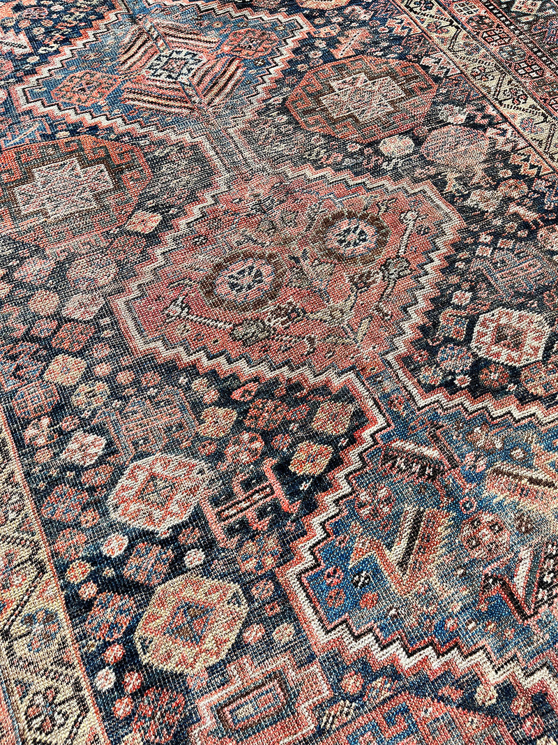 an antique shiraz qashqai rug with a dark blue field and brick red medallions