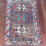 an antique caucasian rug with red and blue accents and a large geometric pattern