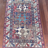 an antique caucasian rug with red and blue accents and a large geometric pattern