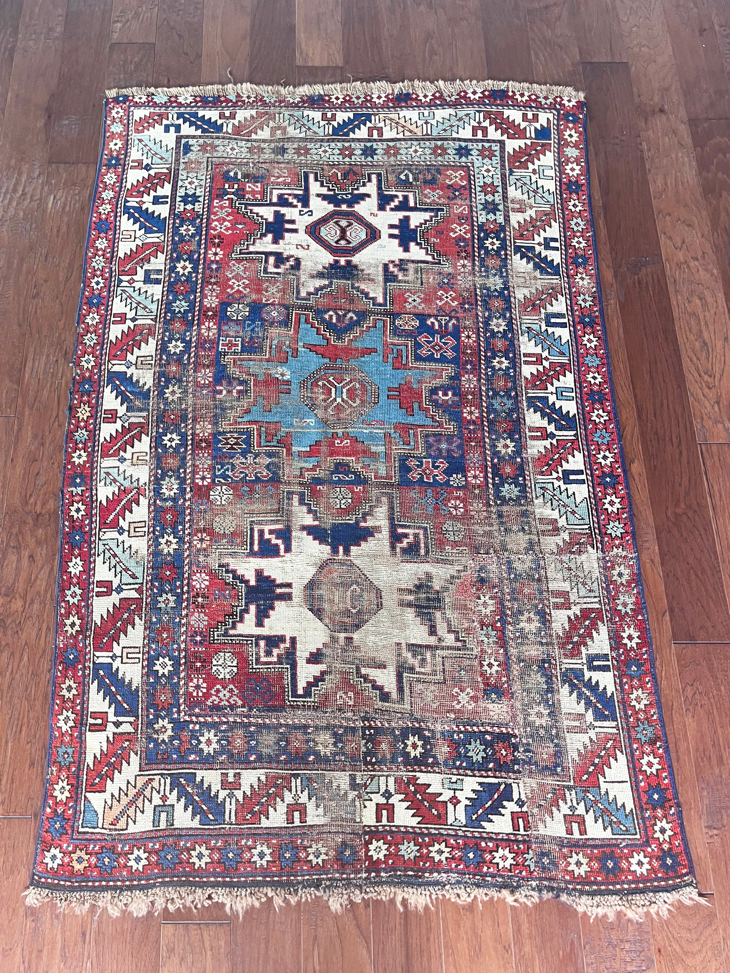 an antique caucasian rug with red and blue accents and a large geometric pattern
