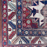 an antique caucasian rug with red and blue accents and a large geometric pattern