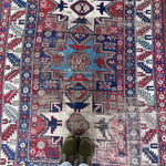 an antique caucasian rug with red and blue accents and a large geometric pattern