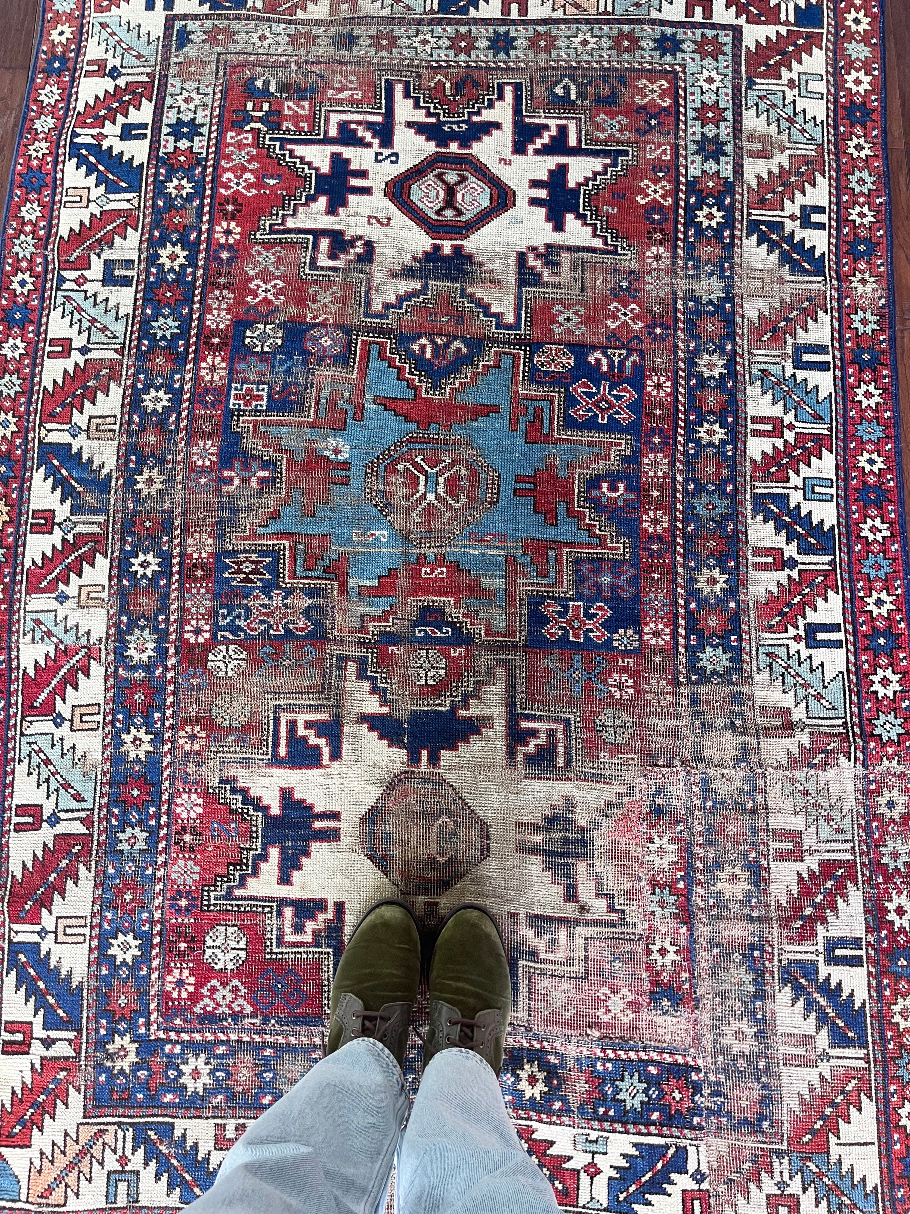 an antique caucasian rug with red and blue accents and a large geometric pattern