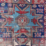 an antique caucasian rug with red and blue accents and a large geometric pattern