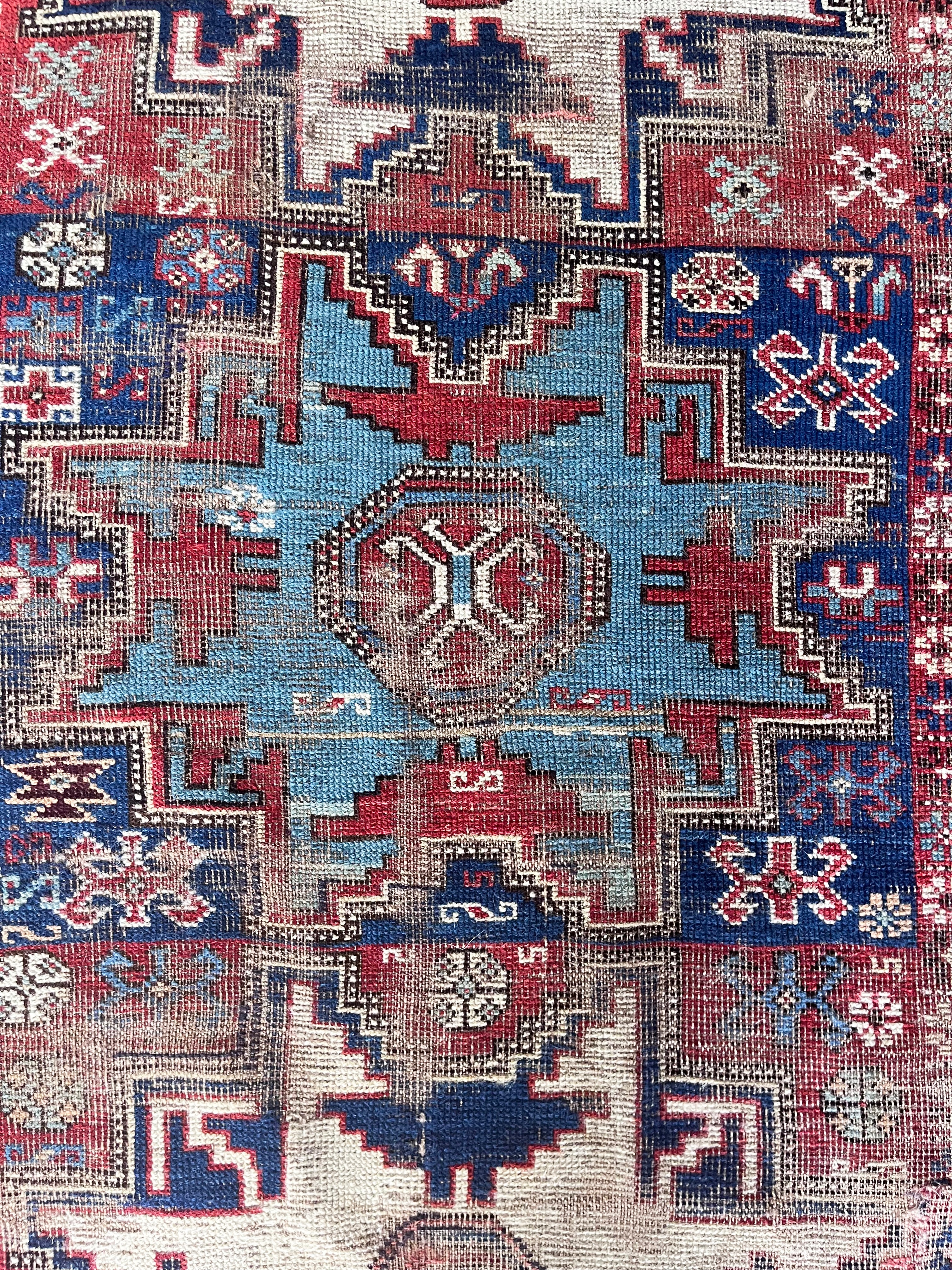 an antique caucasian rug with red and blue accents and a large geometric pattern