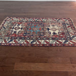 an antique caucasian rug with red and blue accents and a large geometric pattern