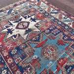 an antique caucasian rug with red and blue accents and a large geometric pattern