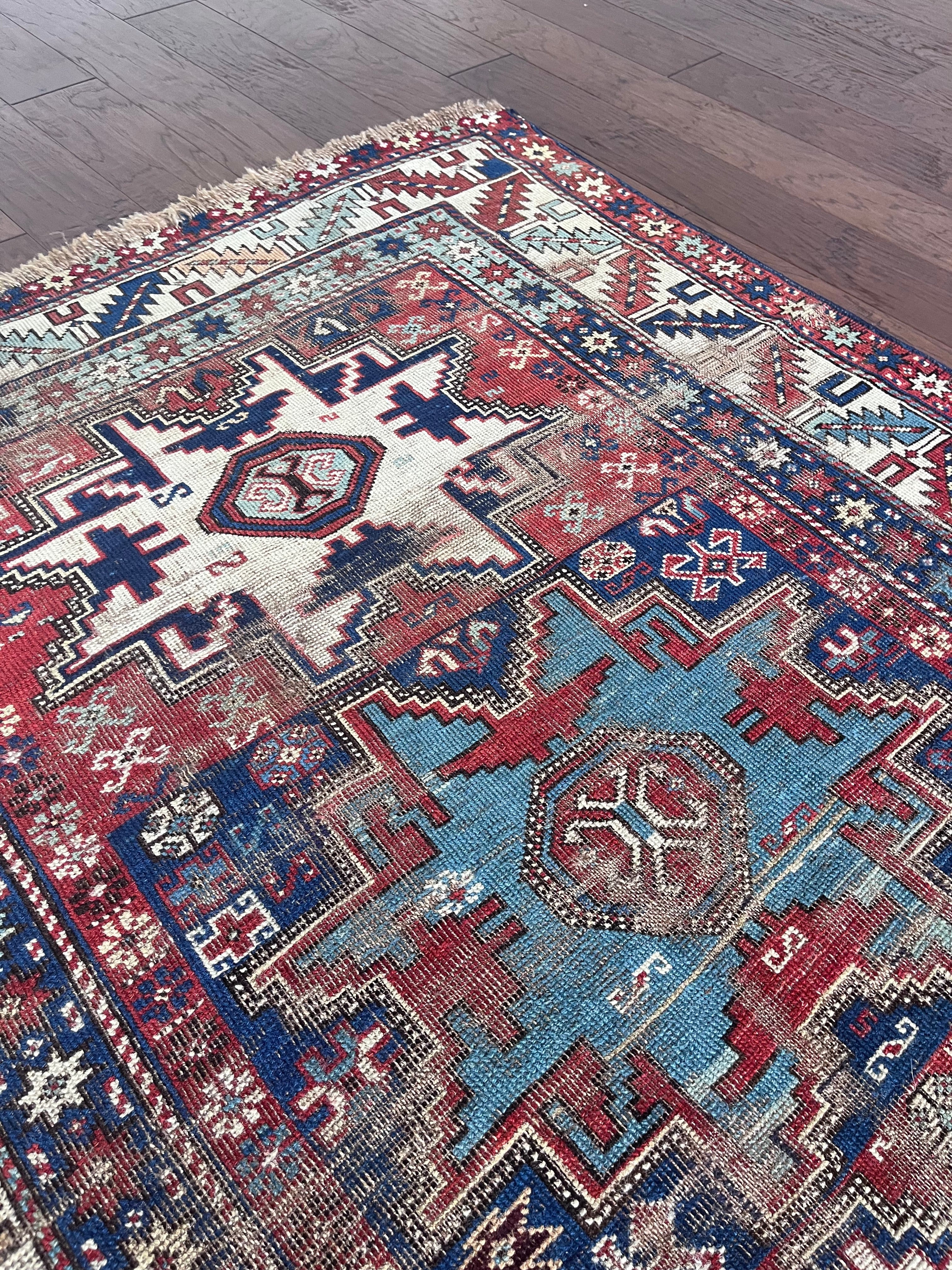 an antique caucasian rug with red and blue accents and a large geometric pattern